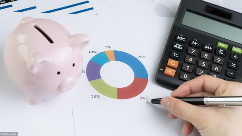 Finance, Money Budget Planning Or Investment Asset Allocation Concept, Hand Holding Pen Reviewing Pie Chart And Graph With Calculator And Pink Piggy Bank On Table