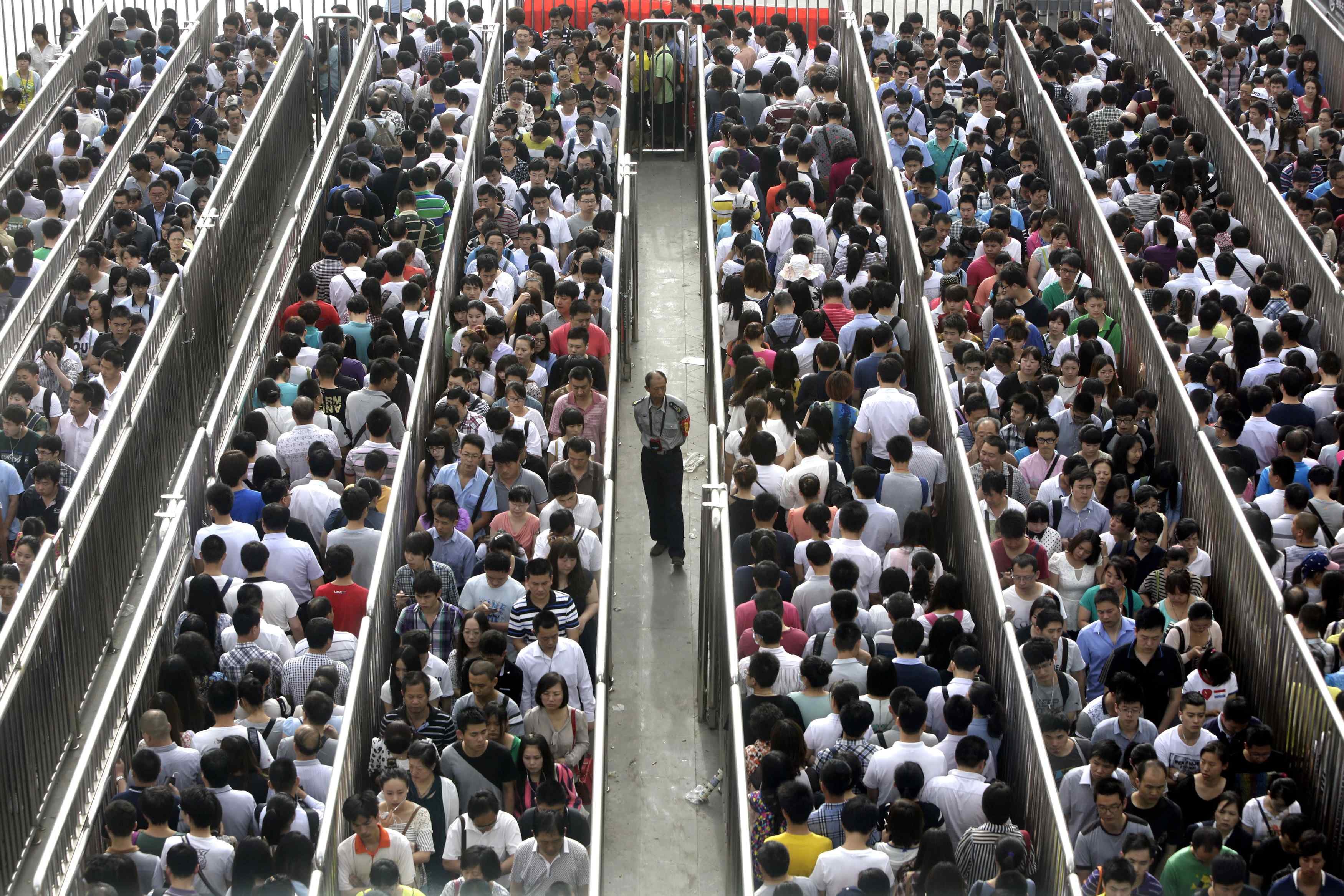 Image: A security officer stands guard as passengers line up and wait for a security check during morning rush hour at Tiantongyuan North Station in Beijing